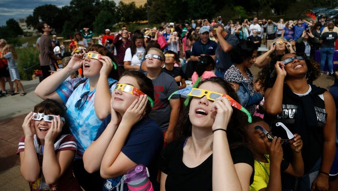Eclipse watchers look up as the clouds break and the beginning of the eclipse starts to become visible Monday, Aug. 21, 2017, during a solar eclipse watch party hosted by the Science Center of Iowa outside the Iowa State Capitol in Des Moines.